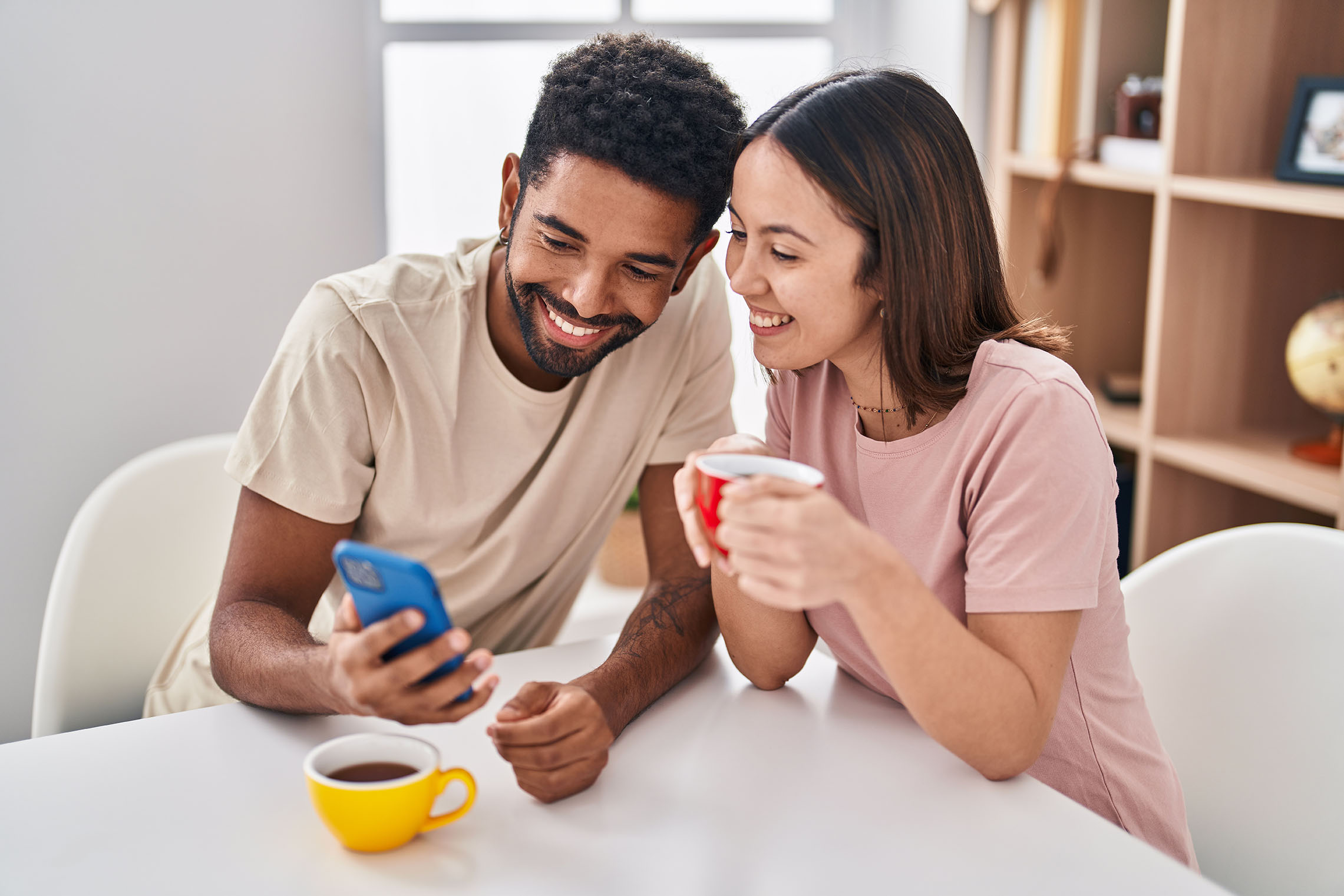 Man and woman couple sitting on table drinking coffee using smartphone at home